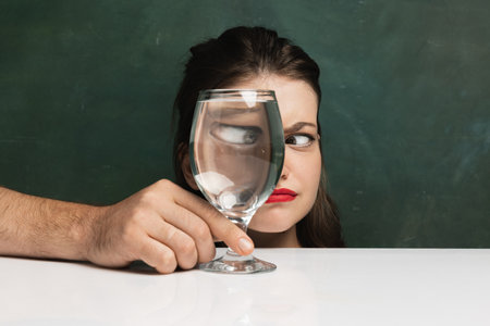 Creative art photography. Beautiful girls face through wine glass over dark green background. Object distortion, optical illusion. Minimalistic contemporary art.の写真素材