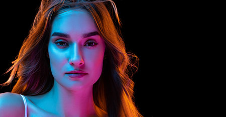 Young beautiful girl with curly long hair isolated over dark blackground in neon light. Looks happy...