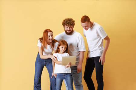 Friendly family, redhead young men, woman and kid wearing casual style clothes using tablet, doing...