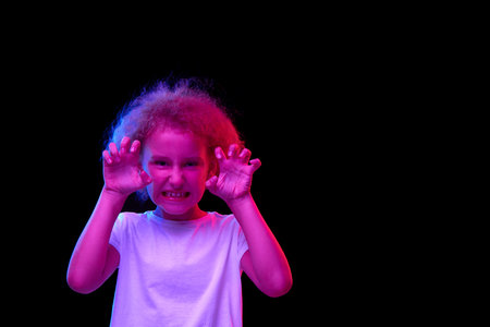 Child is angry. Little girl, kid in white t-shirt isolated over dark background in pink neon light....