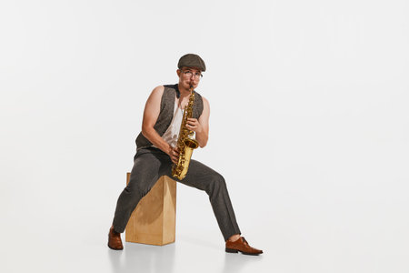 Young musician in retro style outfit playing saxophone isolated over white studio background....
