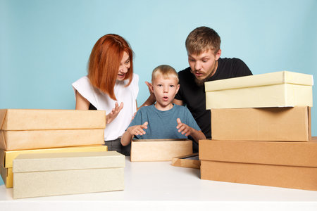 Unpacking. Friendly family, parents and child open cardboard boxes, receive parcels unpack after online shopping over blue background. Black Friday conceptの写真素材
