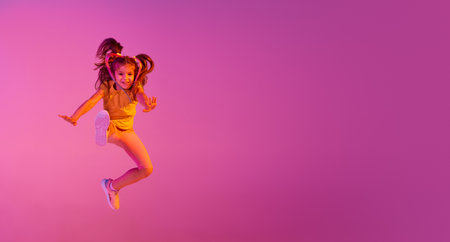 Beautiful active little girl, kid jumping, dancing isolated over pink background in neon. Action, dance, happy childhoodの写真素材