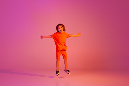 Portrait of caucasian little boy, kid in casual bright clothes dancing isolated over pink background in neon. Action, dance, happy childhoodの写真素材