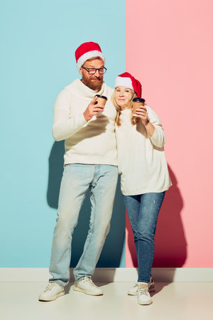 Young charming couple wearing christmas hats and white warm sweaters tasting coffee. Romantic...