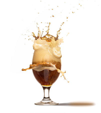 Ice cube falling into beer glass creating huge foam splashes. Glass with dark beer isolated on white...
