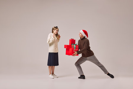 Young and graceful couple of ballet dancers in warm winter clothes dancing with festive gift boxes on grey background. Christmas, New year, holidays, party conceptの写真素材