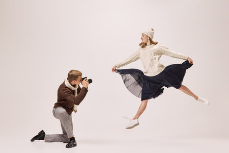 Young stylish photographer taking picture of graceful young ballerina isolated on grey background. Retro, vintage, dance, holidays, party conceptの写真素材
