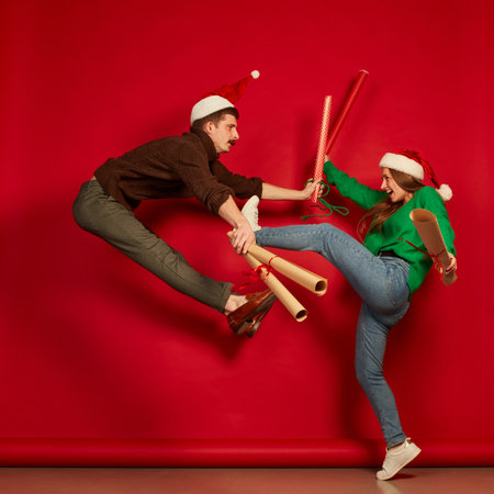 Portrait of cheerful young people, man and woman jumping with wrapping presents paper isolated over red backgroundの写真素材