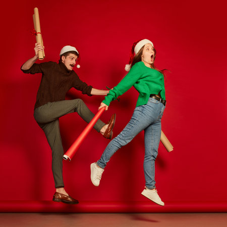 Portrait of cheerful young people, man and woman with wrapping presents paper isolated over red background. Funny emotionsの写真素材