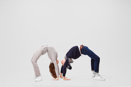 Bridge of understanding. Flexible girl and boy, ballet dancers in warm clothes and hats doing bridges isolated on gray background.の写真素材