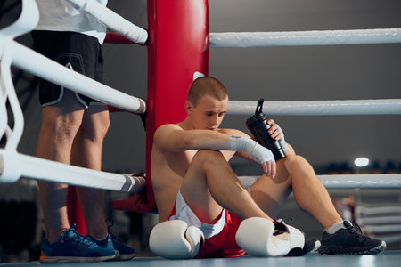 Pre-fight consultation. Young boxer training with personal coach, trainer at boxing ring at sports gym. Sport, strategy, studying, skills and achievementsの写真素材