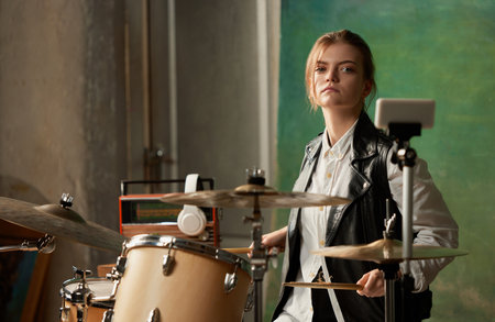 Emotional young girl, rock musician recording music video blog home lesson, playing drums or making broadcast internet tutorial while sitting at record labelの写真素材