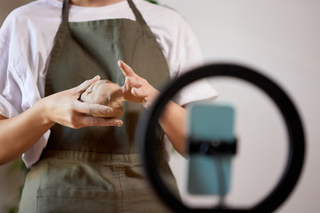 Clay modeling process, learning the basics of pottery. Cropped image of female pottery master with supplies recording vlog at home studio.の写真素材