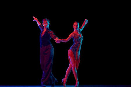 Stylish ballroom dancers couple in gorgeous outfits dancing in sensual pose on dark background in neon light. Concept of art, music, dance, emotions.の写真素材