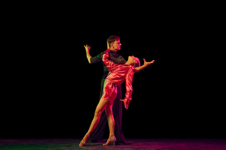 Full-length portrait of young beautiful man and woman dancing ballroom dance isolated over dark background in neon light. Concept of art, beauty, grace, action, emotions.の写真素材