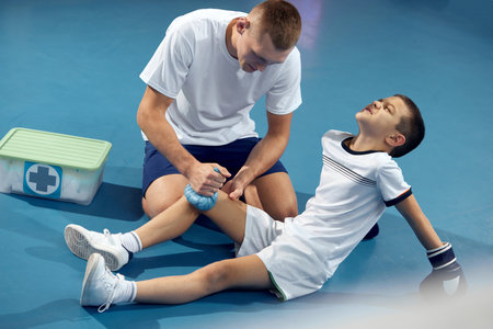 Personal coach, team trainer provides first aid to an athlete with a leg injury. Boxing training in the gym. Sport, medicine, studyingの写真素材