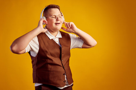 Happy smiling boy in retro costume listening to music in headphones isolated over orange color background. Vintage fashion, music, youth, emotionsの写真素材