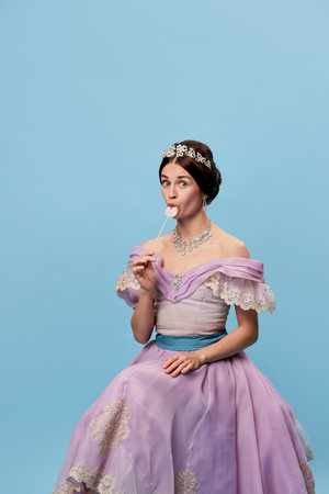 Flirt. Portrait of sensual young girl in lilac color medieval dress as young queen or princess tasting lollipop. Eras comparison, beauty, art, emotions and vintage fashion styleの写真素材