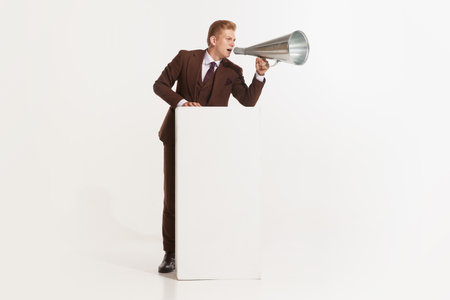 Full length view of young employee businessman in classic formal retro suit screaming hot news in megaphone isolated on white background studio. Concept of speaker, communication, leadershipの写真素材