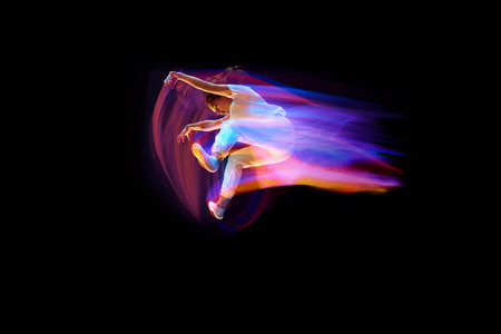 In miracle flight. Young sportive dancer in white clothes levitating, moving over dark background in...