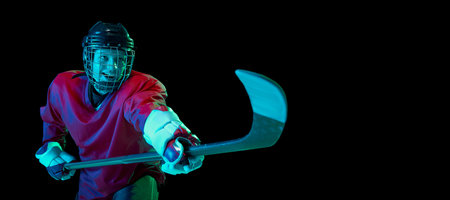 Powerful throw. Male ice hockey player in sports protective uniform in action over dark background in neon light. Sport, power, challenges, achievement, goalsの写真素材