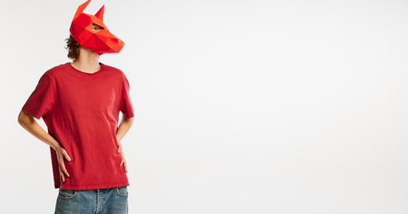 Young man in red t-shirt with cardboard animal mask on his head isolated on white background. Concept of art, fashion, theater, funny meme emotions.の写真素材
