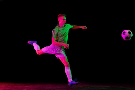 Young professional male football soccer player in motion isolated on dark background in neon light....