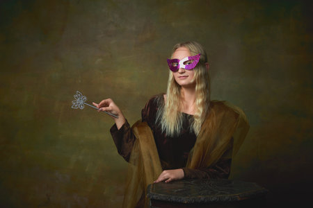 Mask ball. Portrait of young girl as Mona Lisa picture posing over dark vintage background. Retro style, art, fashion, comparison of eras concept.の写真素材