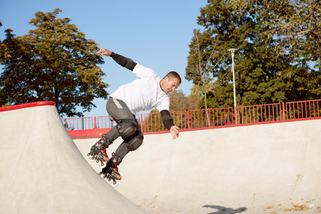 Energetic man on roller skates in motion at modern roller skate park. Roller skater doing dangerous...
