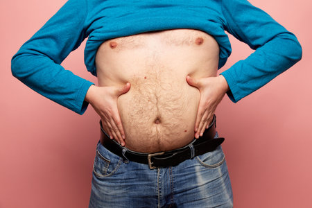 Cropped image of fat man showing his belly, abdomen. Close up part of mans body. Concept of dieting, sport, fitness, healthy lifestyle, body positiveの写真素材
