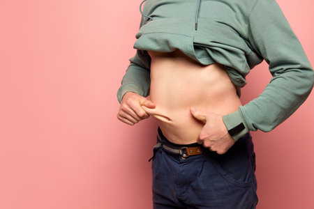 Closeup male hands stretching skin on his belly, man showing to camera his abdomen. Concept of dieting, sport, fitness, healthy lifestyle, body positive and wellbeingの写真素材