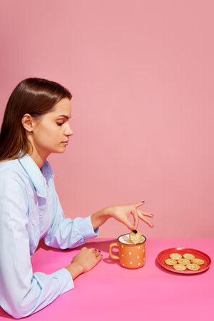 Goodies. Food pop art photography. Young girl tasting milk with crackers isolated over pink background. Concept of food, creativity.の写真素材