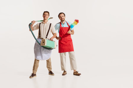 Portrait of two men in aprons with vacuum cleaner and pipidastre isolated over white background. Male cleaning serviceの写真素材