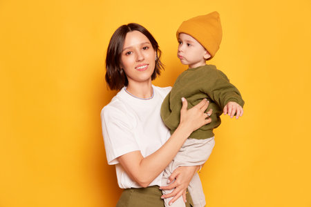 Happy young mother with her cute little son posing isolated on bright yellow background. Family,...