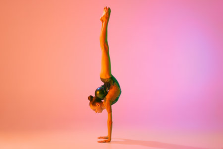 Studio shot of young charming girl, rhythmic gymnast training with sports equipment isolated over...