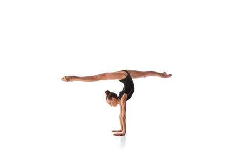Twine in hand stand. Portrait of junior gymnast in black sport swimsuit doing gymnastics excercises...