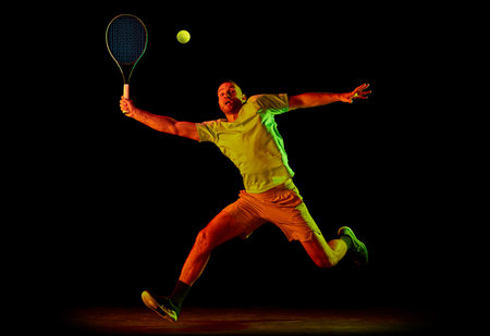 Studio shot of professional tennis player playing tennis isolated over dark background in neon light. Concept of motion, speed, professional sport.の写真素材