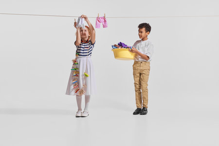 Portrait of cute little children, boy and girl hanging clothes to dry isolated over grey studio backgroundの写真素材