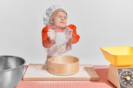 Cute little child, girl in image of chef cooking over grey background. Sifting flour, dirty faceの写真素材