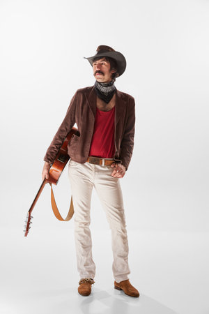 Portrait of man with moustaches in country style vinatge clothes posing with guitar isolated over white background. Live performerの写真素材