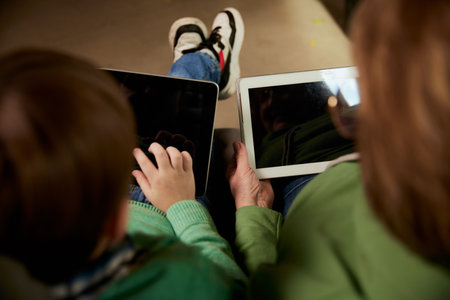 Back view of grandmother and grandson spending time together, using tablets at home. Concept of...