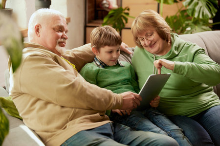Life portrait of friendly family, grandparent and their grandson sitting on sofa and spending time...
