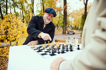 Portrait of senior man playing chess in the park on a daytime in fall. Looking happy. Concept of leisure activity, old generationの写真素材