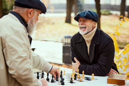 Portrait of two senior men playing chess in the park on a daytime in fall. Happy and delightful....