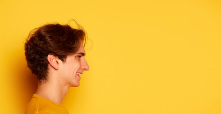 Side view portrait of young man with curly hair posing isolated over yellow background. Concept of youth culture, emotionsの写真素材