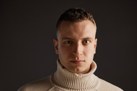 Portrait of handsome man posing in stylish sweater isolated over dark grey studio background....