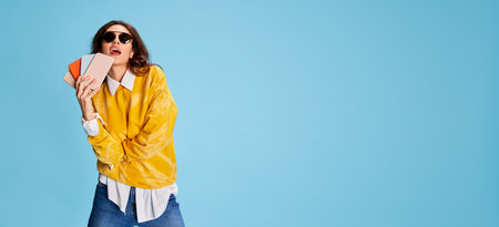 Portrait of young beautiful girl posing with phones isolated over blue background. Shopping, big sales on gadgets. Flyerの写真素材