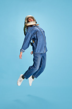 Portrait of young beautiful girl posing in uniform and astronaut helmet isolated over blue...