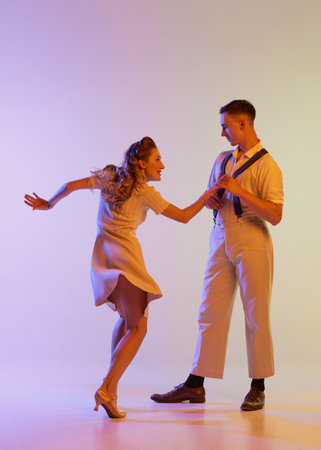 Incendiary dance. Emotional couple of dancers in retro style outfits dancing social dances isolated on gradient lilac color background in neon light. Concept of art, 60s, 70s cultureの写真素材